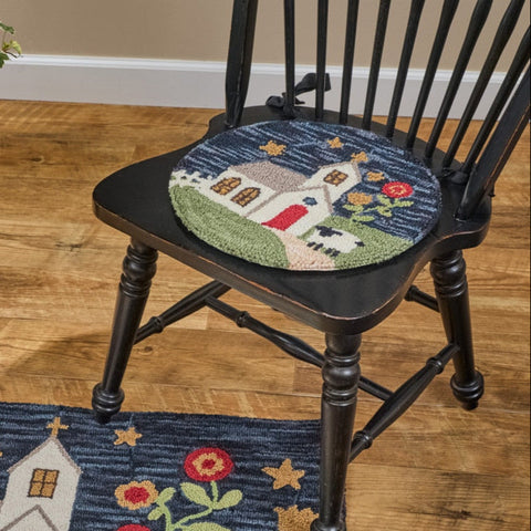 Chapel On The Hill Hooked Chair Pad with a whimsical church, flowers, sheep, and path design shown on a black wooden chair