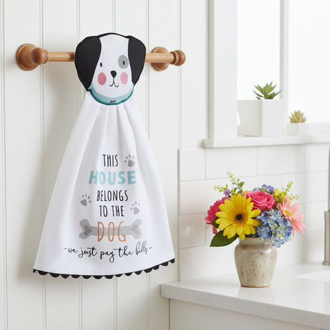 A white dog-themed kitchen towel with a printed cartoon dog face at the top and the text 'THIS HOUSE BELONGS TO THE DOG - we just pay the bills -' with paw prints and a bone graphic.