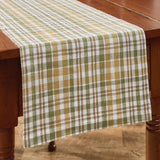 Sage & Mustard Plaid Table Runners draped over a wooden dining table, featuring a pattern of sage green, mustard yellow, putty brown and white intersecting stripes.