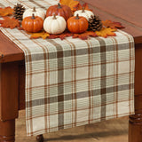 Toffee & Elm Plaid Table Runner 36" draped over a wooden dining table, featuring a cream, brown, and tan checkered pattern with Fall pumpkin leaves and pinecone accents.