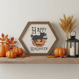 Happy Halloween hexagon wood sign with black cat on jack-o-lantern displayed on a farmhouse shelf with mini pumpkins, fall leaves, wheat stems, and a lantern