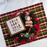 Small Town Christmas wood sign styled overhead on a red plaid runner with a red charger plate, Santa ornaments, pinecones, and red berries
